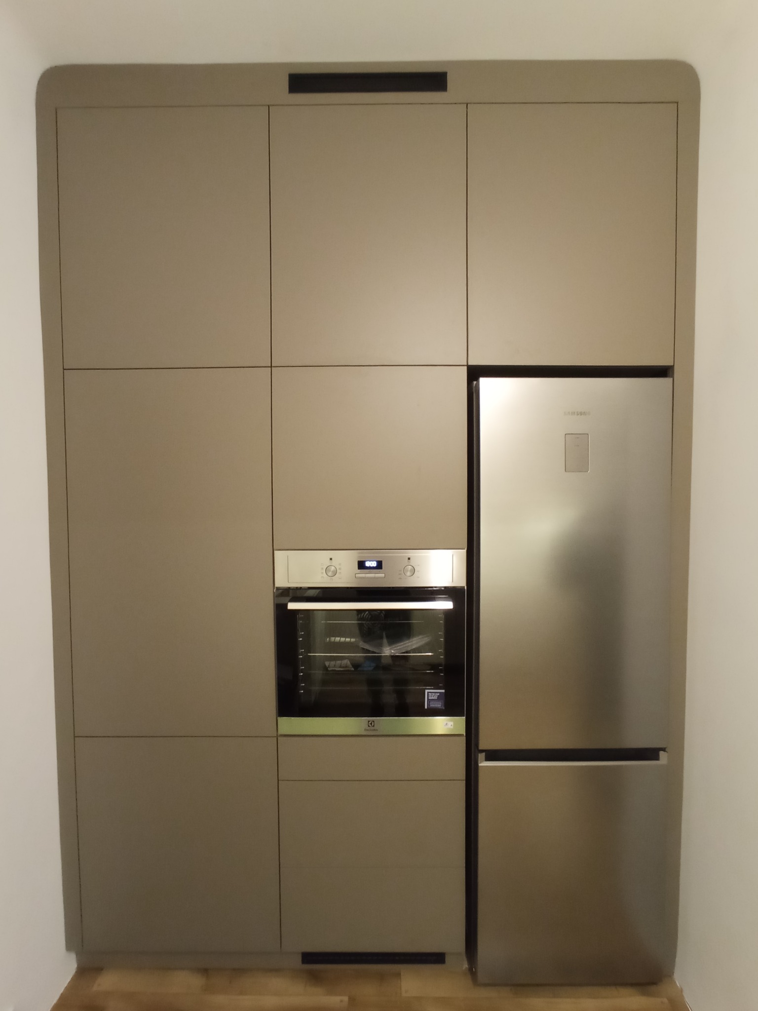 Zabudowa kuchenna w kolorze taupe z piekarnikiem Electrolux i lodówką Samsung, minimalistyczny design z zaokrąglonymi krawędziami szafek.