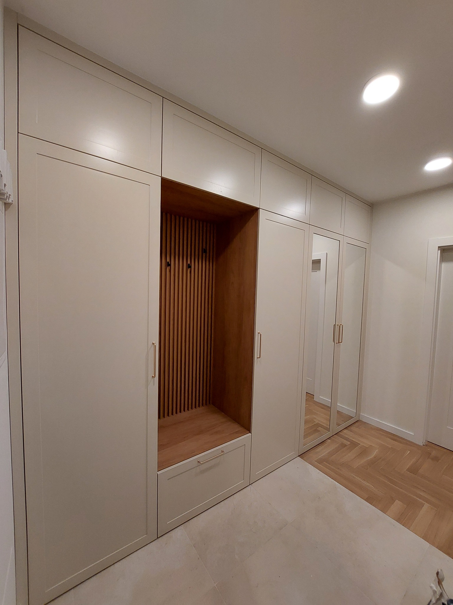 Beżowa szafa wnękowa z drewnianą wnęką na buty i wieszakami, lustrzane drzwi, parkiet jodełka