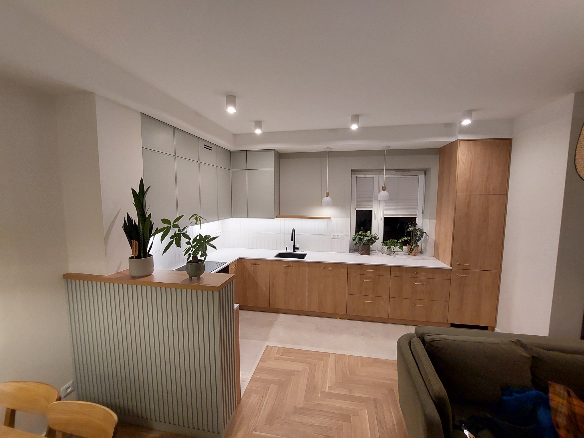 Nowoczesna kuchnia z drewnianymi frontami i szarymi szafkami wiszącymi, uzupełniona o rośliny doniczkowe na blacie i wyspie, zrealizowana w Zielonce.