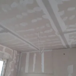 Sufit i ściany w trakcie montażu płyt kartonowo-gipsowych, widoczne profile, łączenia płyt zaszpachlowane, wystające przewody elektryczne.