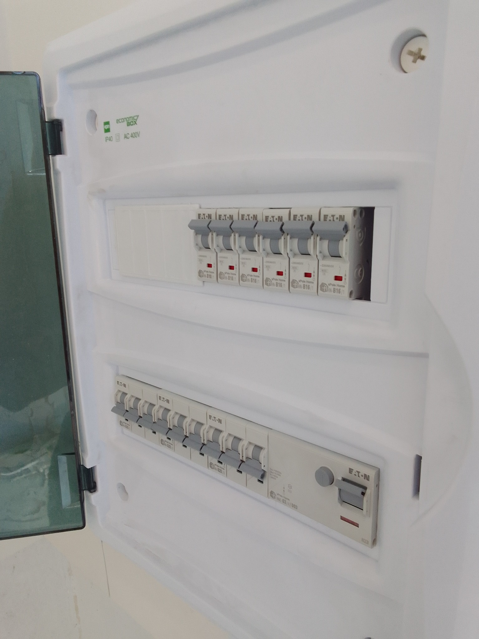 Otwarta skrzynka elektryczna z bezpiecznikami EATON, widoczne dwa rzędy wyłączników, górny rząd z wyłącznikami jednofazowymi, dolny rząd z wyłącznikami trójfazowymi oraz wyłącznikiem...