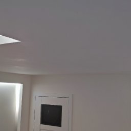 myRemont - Minimalistyczne wnętrze: białe ściany, szary sufit z wbudowanym oświetleniem LED w geometrycznych wnękach, widoczny fragment drzwi.