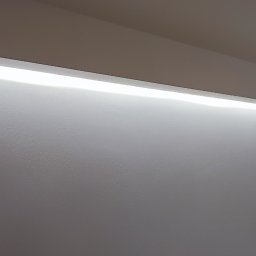 myRemont - Biała ściana z wnęką oświetloną listwą LED, widoczny fragment sufitu i framuga drzwi.