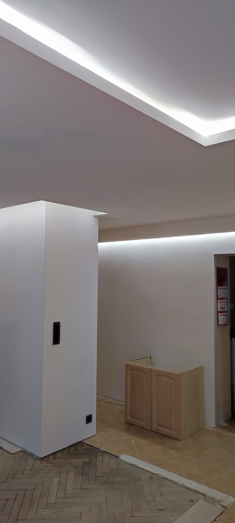 Wnętrze w trakcie remontu: widoczne podwieszane sufity z oświetleniem LED, częściowo ułożony parkiet w jodełkę, niekompletna zabudowa kuchenna i elementy instalacji elektrycznej.