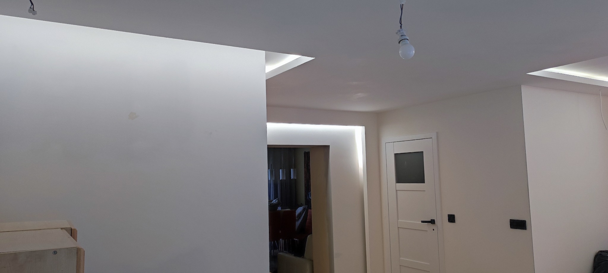 Wnętrze po odświeżeniu z białymi ścianami, widoczne oświetlenie LED w suficie i nad przejściem, drzwi z przeszkleniem i wisząca żarówka bez klosza.