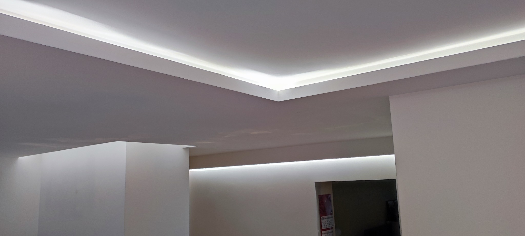 Nowoczesny sufit podwieszany z oświetleniem LED w minimalistycznym wnętrzu, widoczne precyzyjne wykończenie narożników i równomierne rozprowadzenie światła.