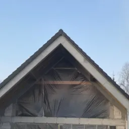 Surowy stan dachu z czarną dachówką na budynku w trakcie budowy w Warszawie, zabezpieczony folią przed dalszymi pracami.