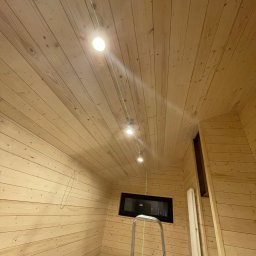 Serhii Haiduchyk - Wnętrze łazienki w trakcie wykończenia, drewniana boazeria na ścianach i suficie, zamontowane oświetlenie punktowe, widoczna drabina i wanna