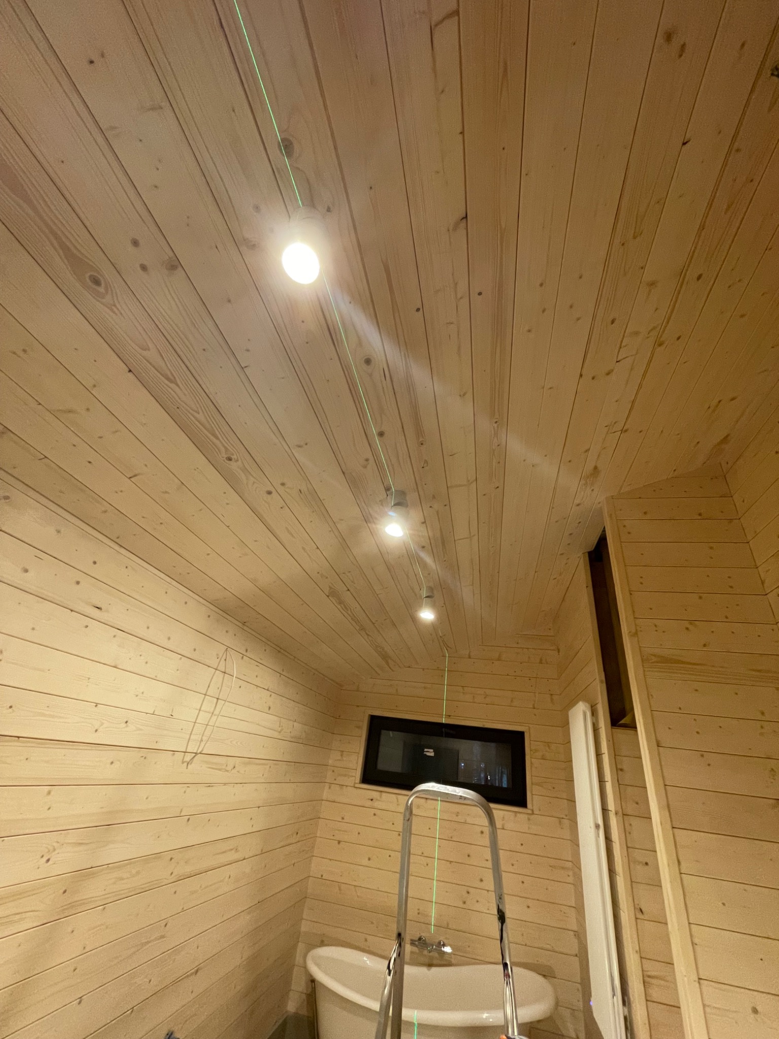 Wnętrze łazienki w trakcie wykończenia, drewniana boazeria na ścianach i suficie, zamontowane oświetlenie punktowe, widoczna drabina i wanna
