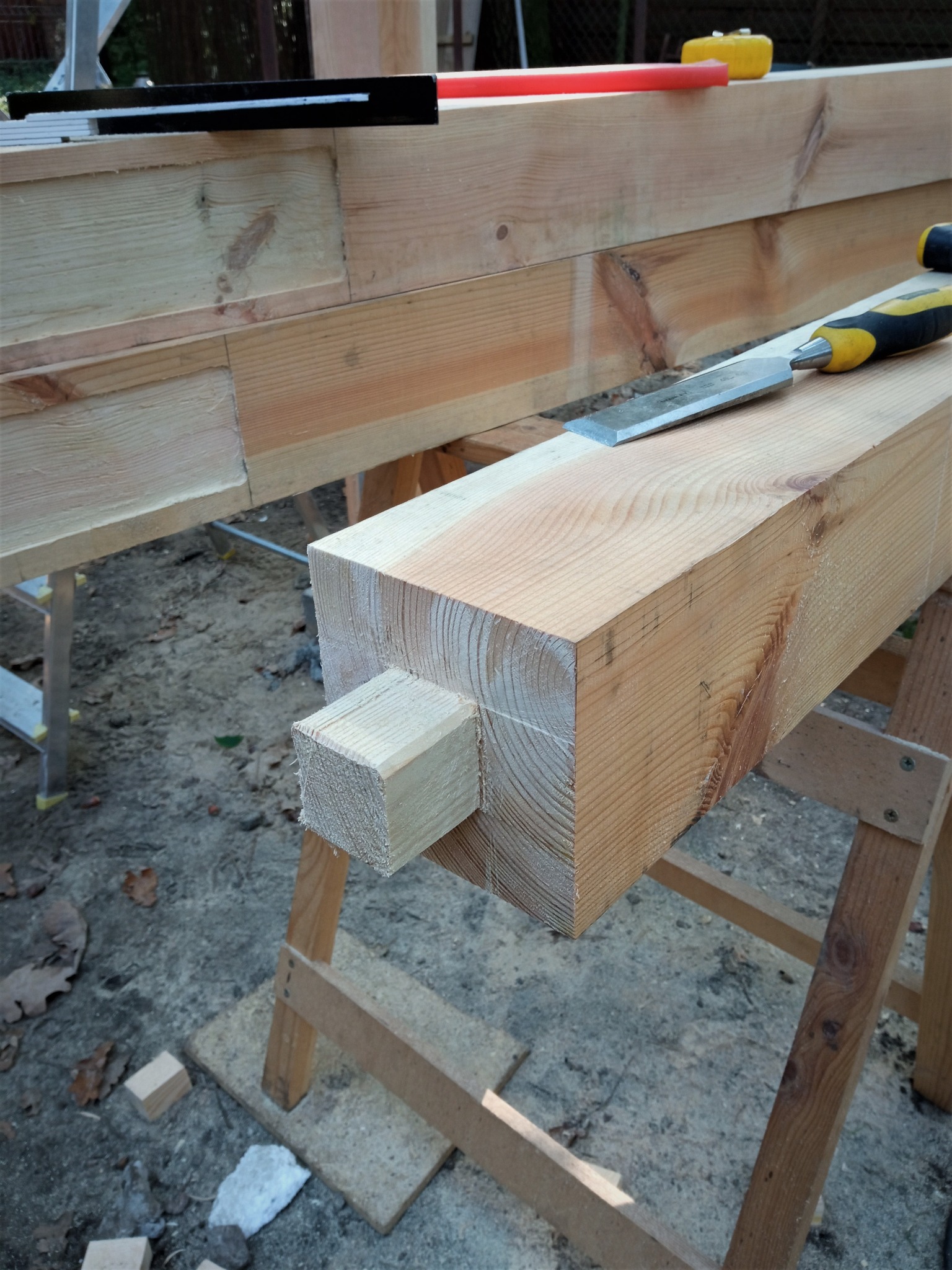 Przygotowanie drewnianej konstrukcji: czopy i gniazda w belkach na kozłach, dłuto na górnej belce, etap obróbki drewna.