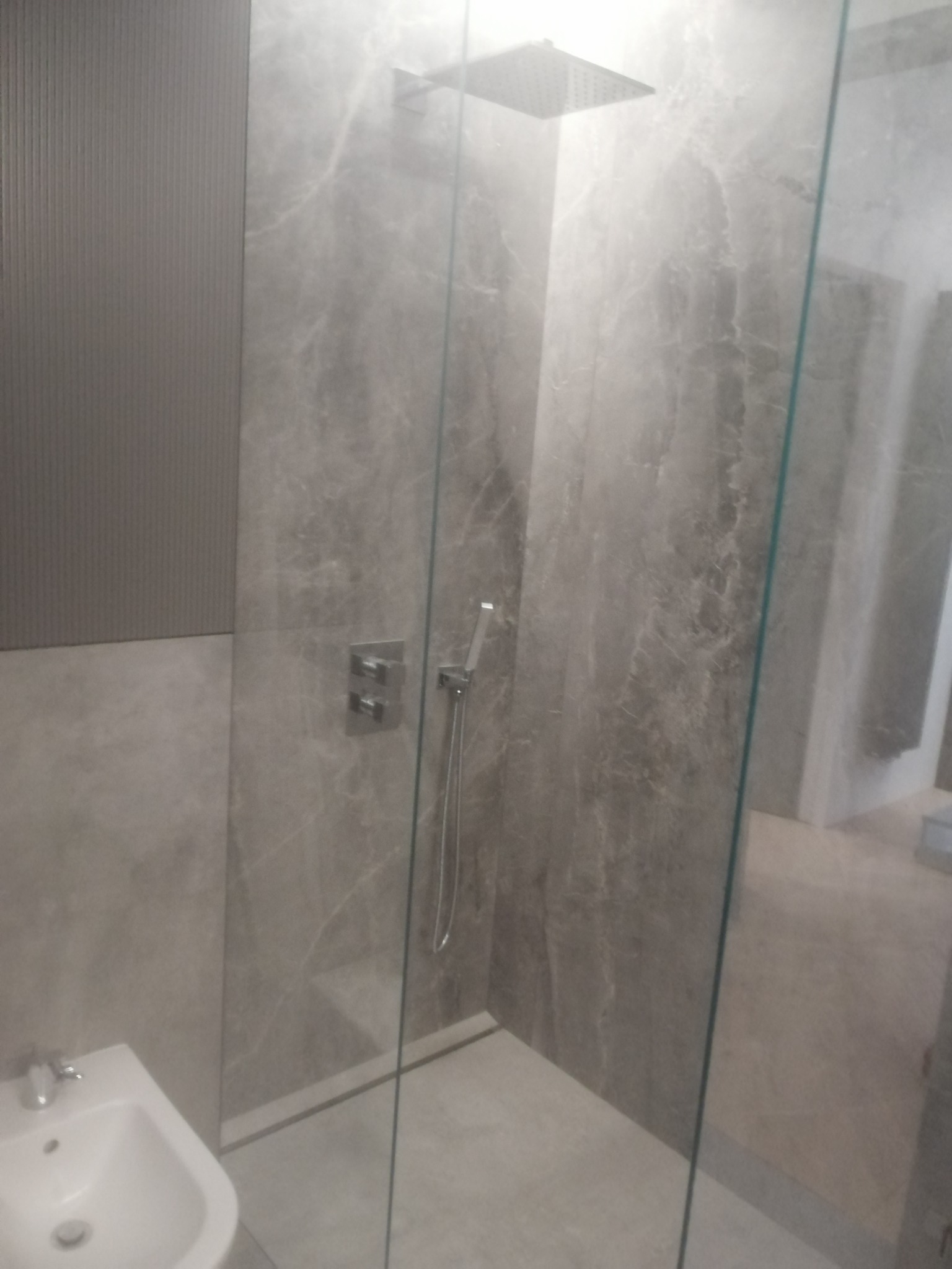 Szara łazienka z kabiną prysznicową typu walk-in, wykończona marmurowymi płytkami, widoczna bateria podtynkowa i deszczownica.