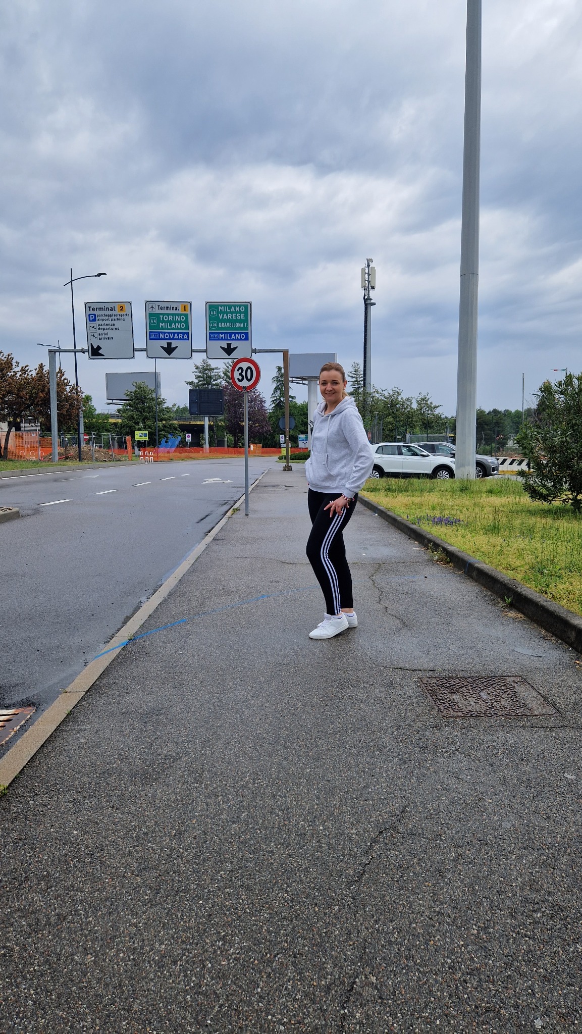 Kobieta w sportowym stroju stoi na chodniku w Białogardzie, w tle znaki drogowe i szary krajobraz.