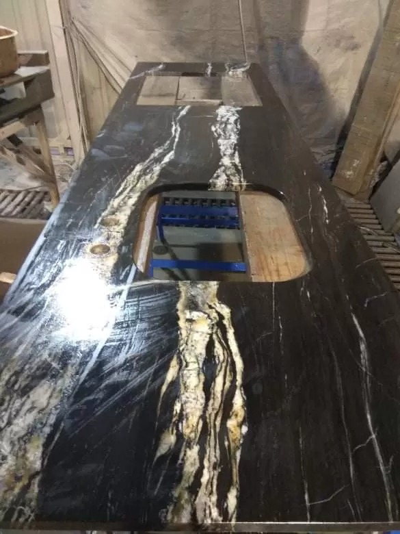 Czarny blat z unikalnym wzorem białych i złotych żył, z wyciętymi otworami na zlew i płytę grzewczą, sfotografowany w warsztacie kamieniarskim.