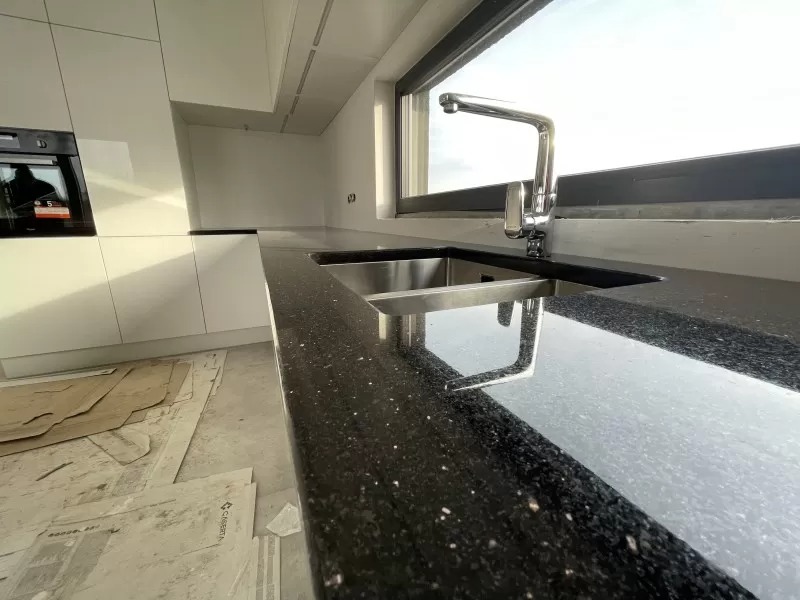 Błyszczący, czarny blat kamienny w kuchni z chromowaną baterią i zlewozmywakiem, widoczne zabezpieczenia podłogi podczas montażu.