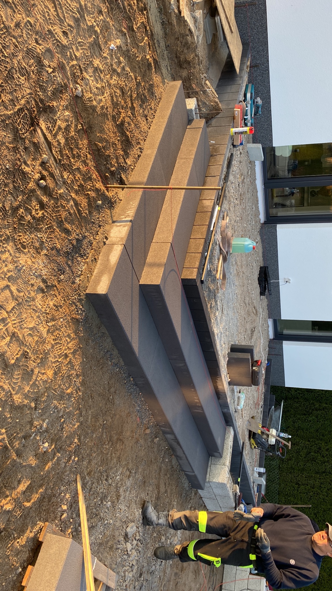 Budowa schodów zewnętrznych z szarej kostki brukowej, widoczne narzędzia i pracownik w ubraniu roboczym.