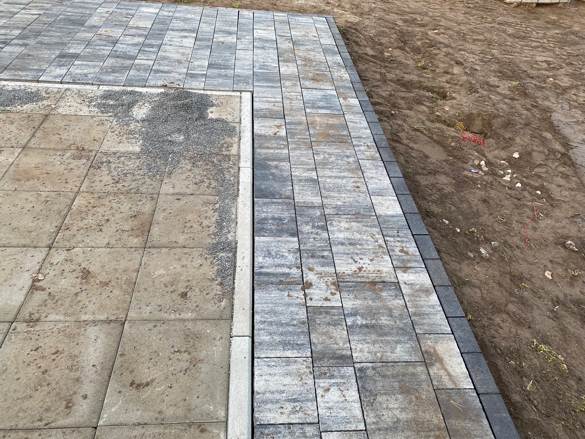 Fragment nowej nawierzchni z kostki brukowej w odcieniach szarości, kontrastujący z obszarem przygotowanym pod dalsze prace i widocznymi elementami gruzu.