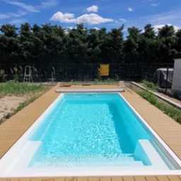 Nowoczesny basen z jasną wodą otoczony tarasem z desek kompozytowych w słoneczny dzień.