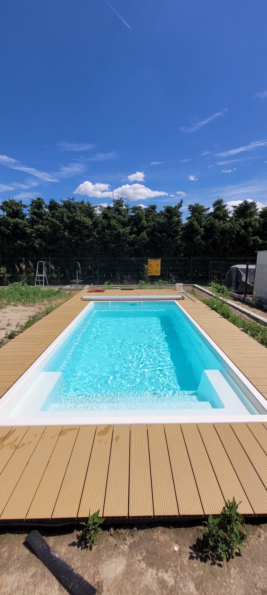 Nowoczesny basen z jasną wodą otoczony tarasem z desek kompozytowych w słoneczny dzień.