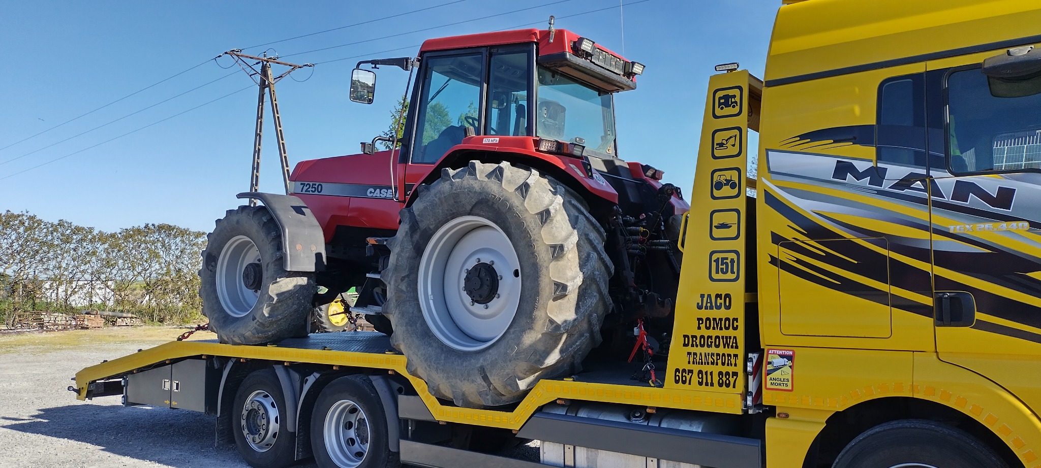 Czerwony ciągnik rolniczy CASE 7250 przewożony na żółtej lawecie MAN pomocy drogowej z napisem JACO Pomoc Drogowa Transport.