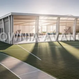 Wizualizacja nowoczesnego budynku z przeszklonymi ścianami na tle zielonego terenu sportowego, widoczne elementy wyposażenia wnętrza i gra światła słonecznego.