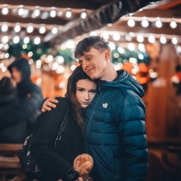 Fotografia Dawid Smułka - Uśmiechnięty mężczyzna obejmuje młodą kobietę z kolczykiem w nosie na tle światełek. Atmosfera intymności i bliskości w ciepłym oświetleniu.