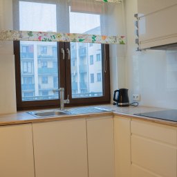 Fotografia Dawid Smułka - Nowoczesna, jasna kuchnia we Wrocławiu z drewnianym blatem i oknem z widokiem na budynek mieszkalny. Minimalistyczny design, czajnik elektryczny na blacie.