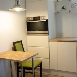 Fotografia Dawid Smułka - Jasna kuchnia z drewnianym blatem i zielonymi krzesłami. Na ścianie wbudowany piekarnik Samsung. Na półce figurka żaby.