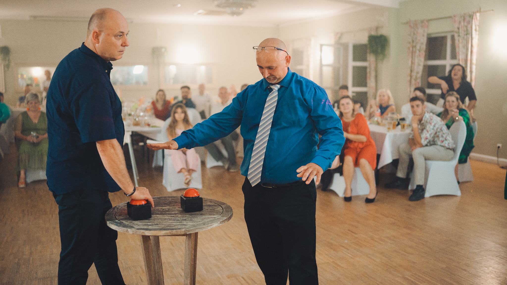 Dwóch mężczyzn w akcji podczas eventu we Wrocławiu. Jeden z nich, w niebieskiej koszuli i krawacie, zamierza nacisnąć czerwony przycisk na stole. Widownia w tle.
