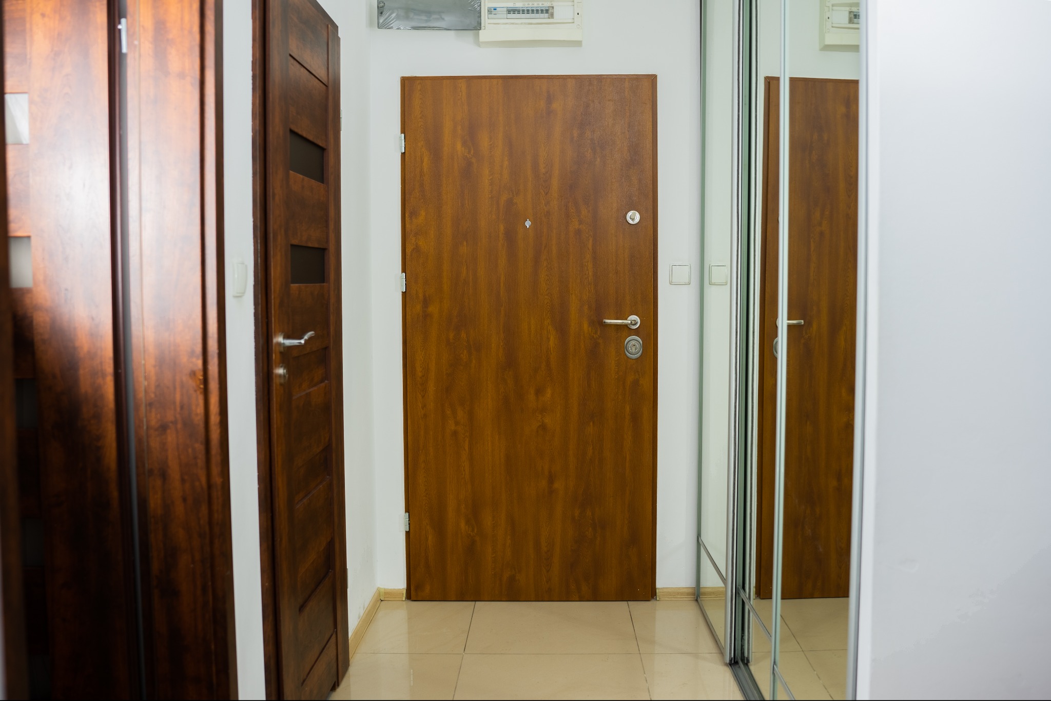 Nowoczesny przedpokój z brązowymi drzwiami wejściowymi i wewnętrznymi z przeszkleniami, oraz szafą z lustrzanymi drzwiami przesuwnymi.