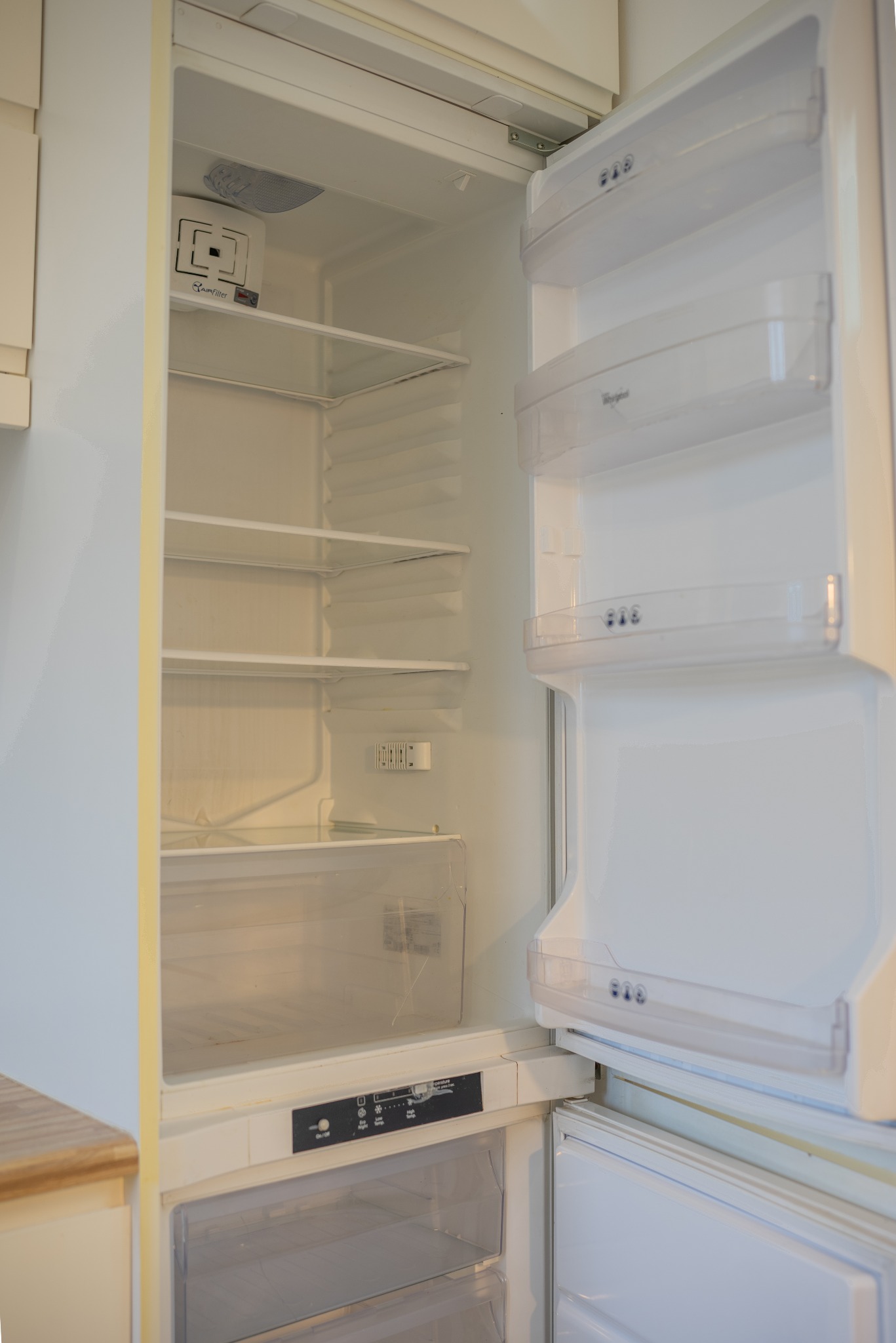 Otwarta, pusta lodówka Whirlpool z widocznymi półkami i szufladami, oświetlona od wewnątrz. Widoczny panel sterowania i filtr powietrza. Ujęcie z bliska, wnętrze lodówki.