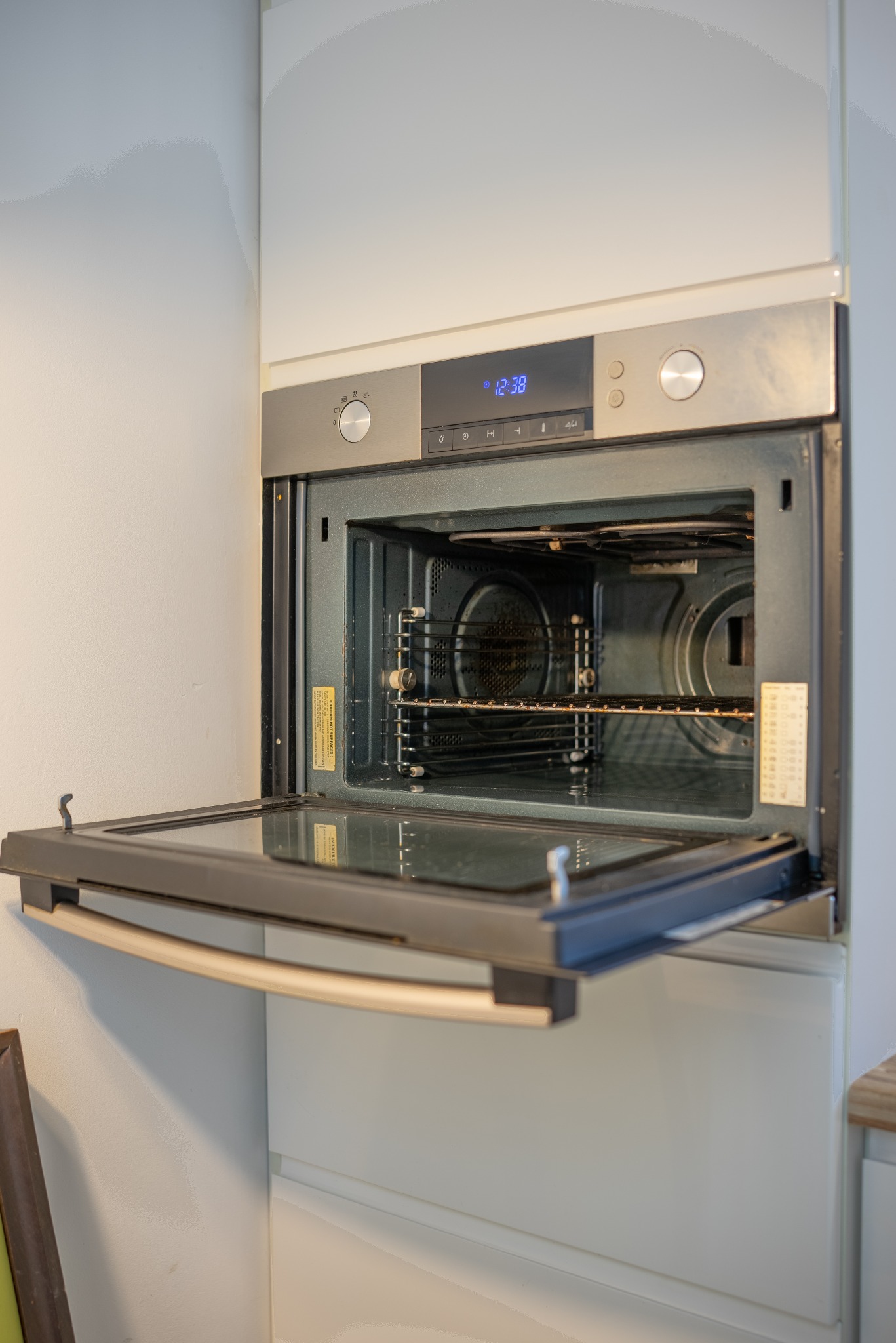 Otwarty piekarnik elektryczny w zabudowie kuchennej, widoczne wnętrze z rusztem i ślady użytkowania. Metalowe wykończenia i cyfrowy wyświetlacz. Ujęcie z bliska.