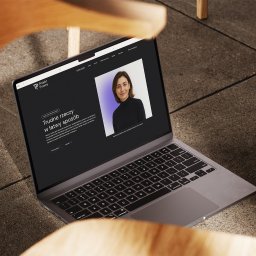 Recreate Sp. z o.o. - Laptop z otwartą stroną internetową 'Projekt Prawny' na tle betonowej posadzki i drewnianych nóg krzesła. Widoczna fotografia uśmiechniętej kobiety i tekst 'Trudne rzeczy w łatwy sposób'.