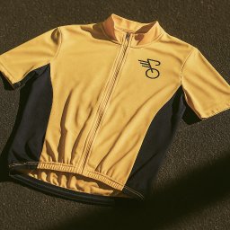 Recreate Sp. z o.o. - Żółto-granatowa koszulka rowerowa z krótkim rękawem i zamkiem błyskawicznym, leżąca na szorstkiej, ciemnej powierzchni w delikatnym oświetleniu.