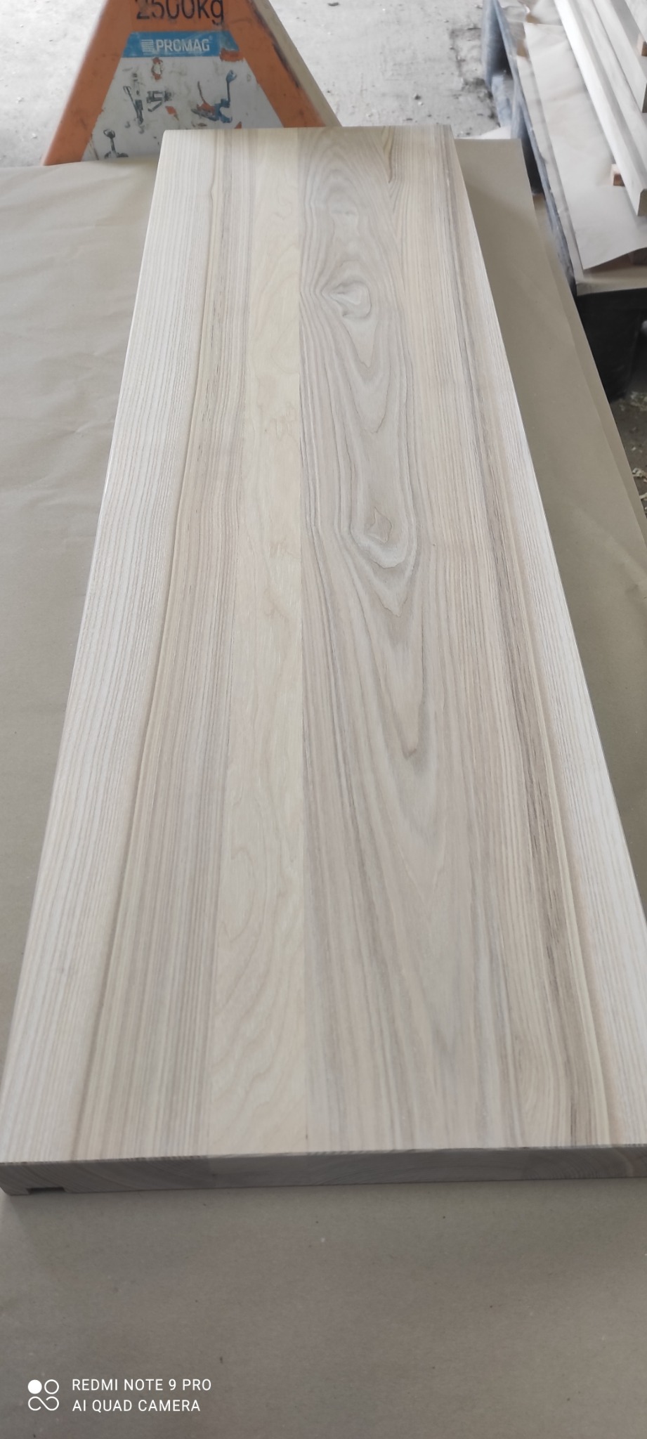 Blat z jasnego drewna z widocznym usłojeniem, przygotowany do dalszej obróbki, leżący na papierze pakowym w warsztacie.