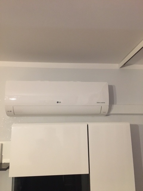Biały klimatyzator LG Dual Inverter zamontowany nad szafkami w pomieszczeniu mieszkalnym.