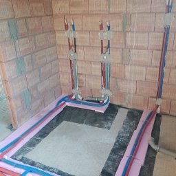 Piotr Sala Hydrosal - Instalacja ogrzewania podłogowego i przyłącza wodno-kanalizacyjnego w surowym stanie, widoczne rury PEX w izolacji termicznej oraz podejścia wod-kan w ścianie z cegły.