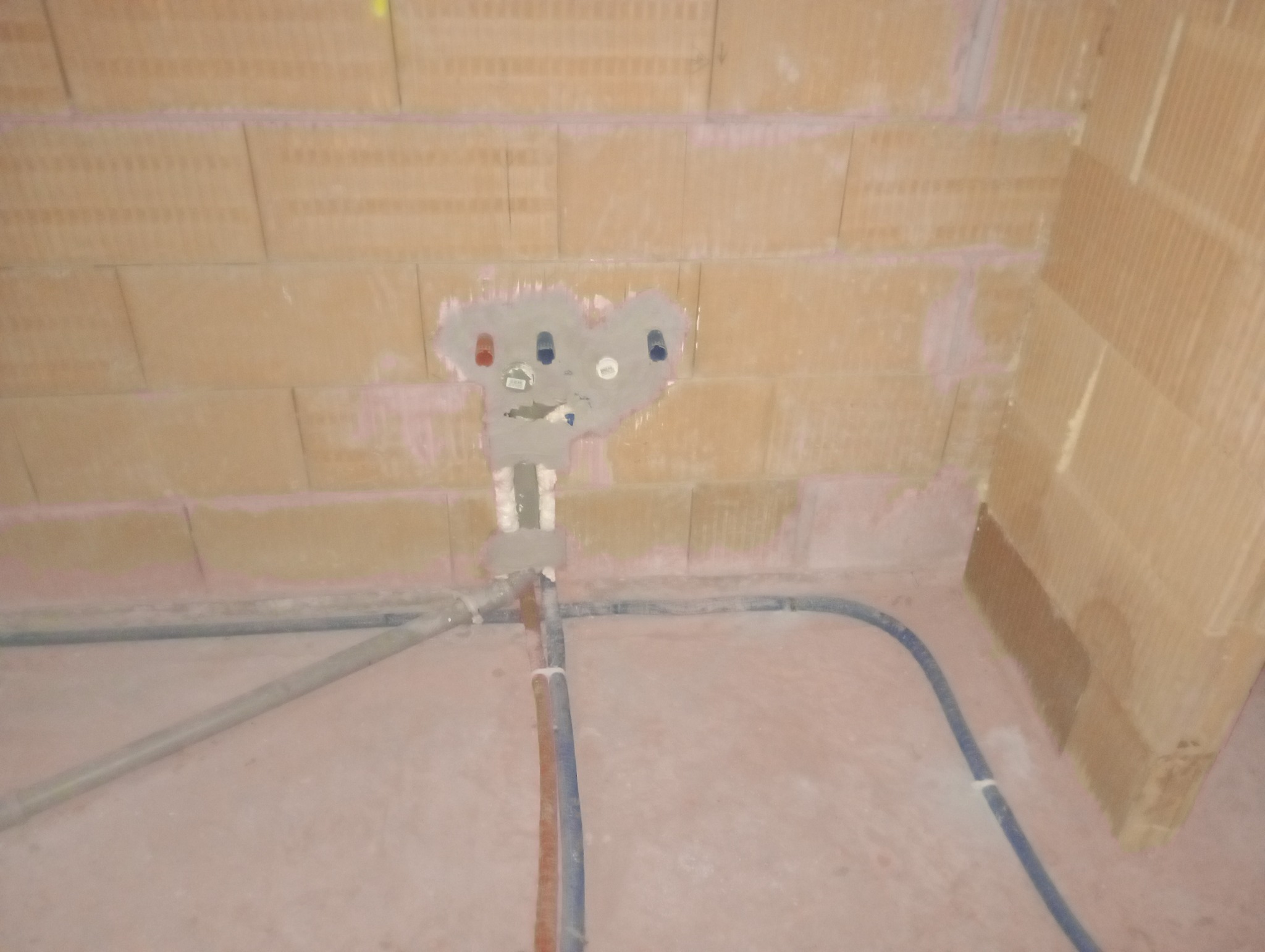 Przyłącze wodociągowe w trakcie montażu w ścianie z cegieł, widoczne rury doprowadzające wodę i częściowo zamurowane podejścia do baterii.