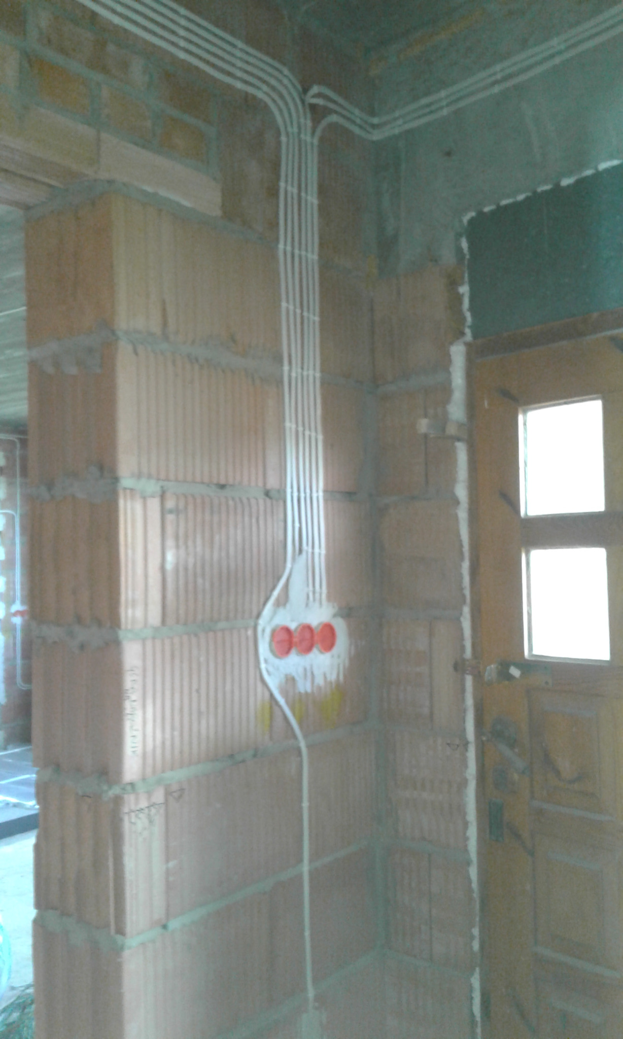 Montaż przewodów elektrycznych w nowym budynku w Sokołowie Małopolskim, widoczne kable prowadzone po ścianie z pustaków i puszka instalacyjna z czerwonymi zaślepkami.