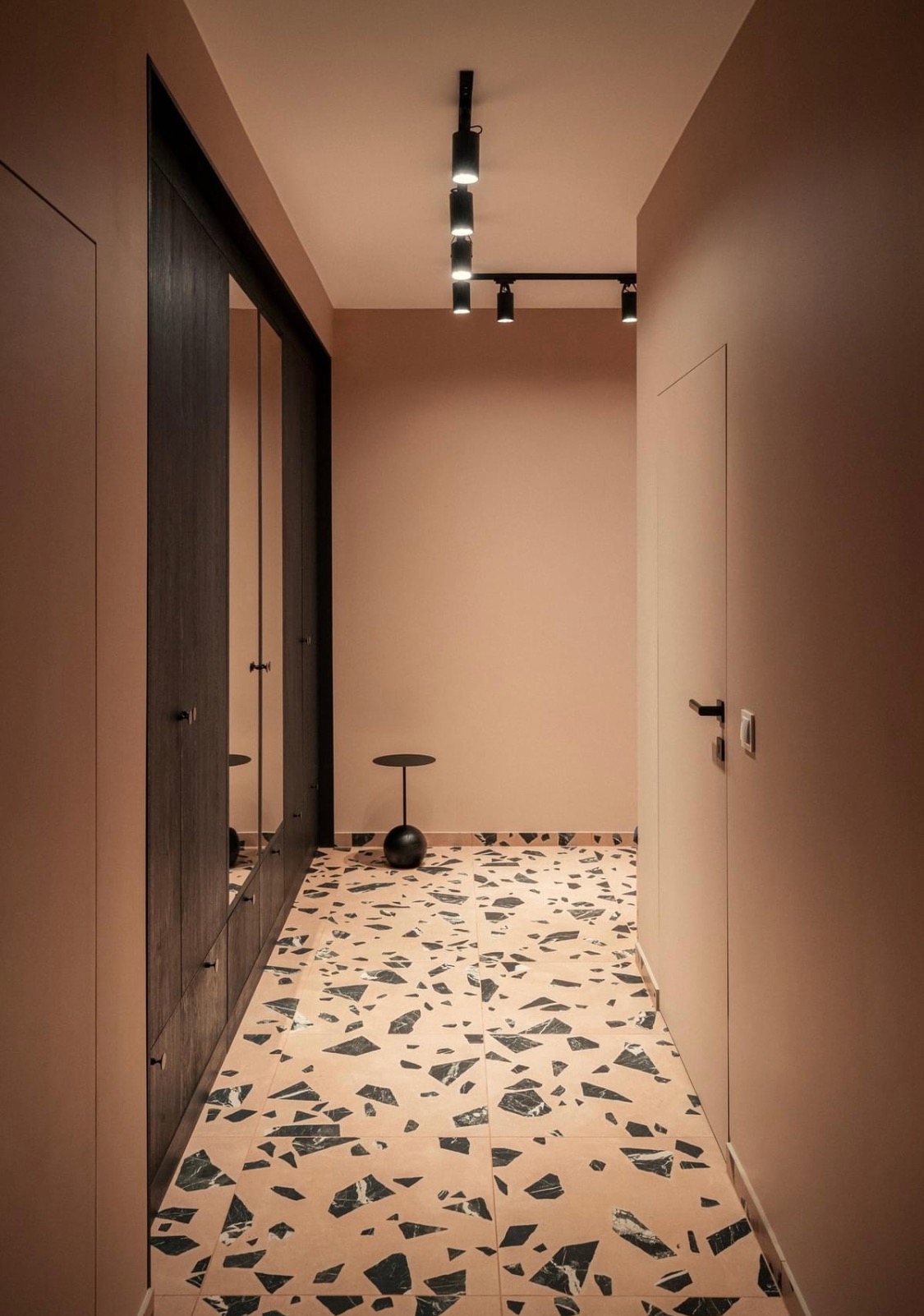 Korytarz w odcieniach różu z terazzo na podłodze, garderoba z lustrami i czarne oświetlenie sufitowe na szynie.
