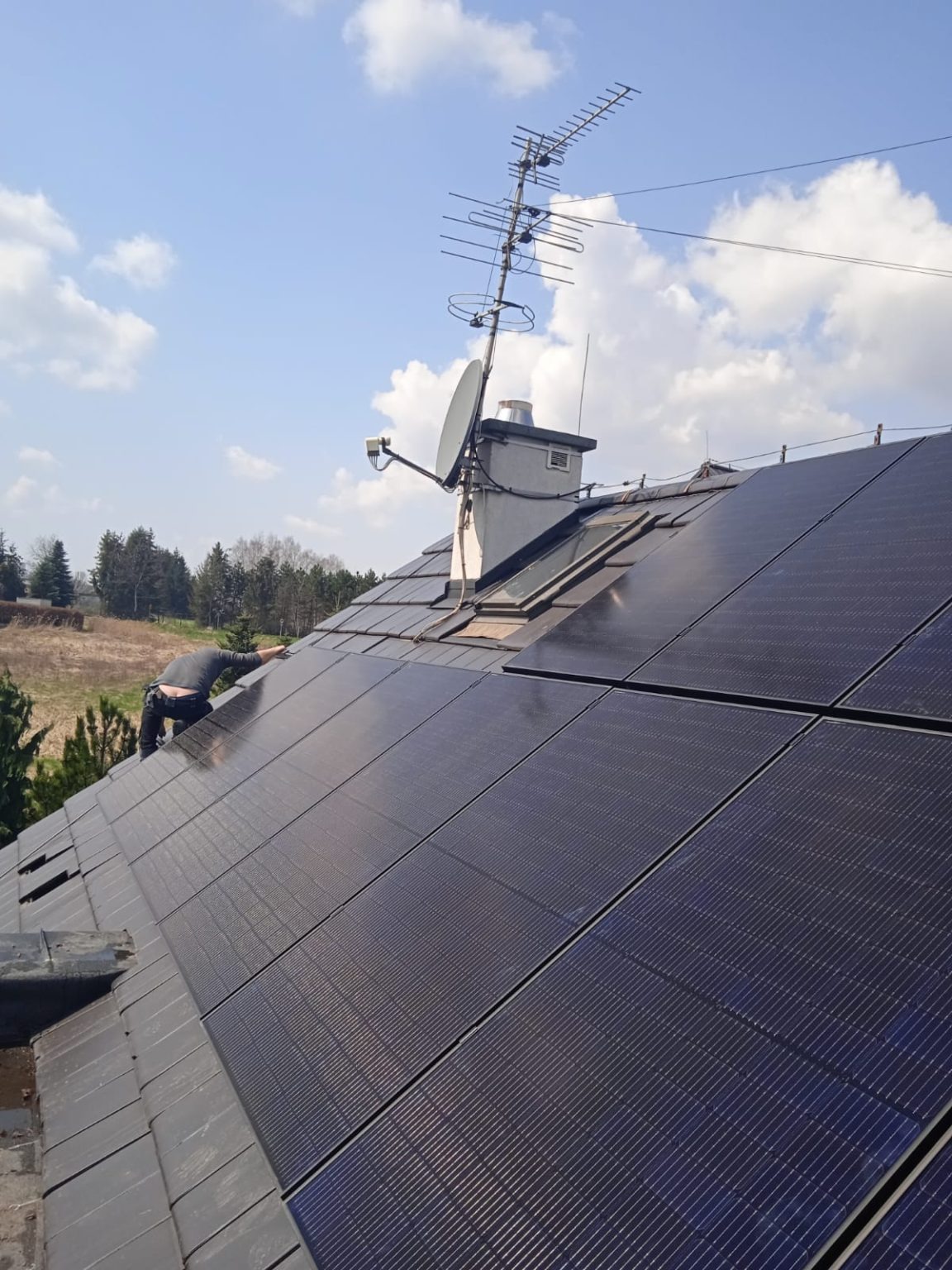 Montaż paneli słonecznych na dachu domu z anteną satelitarną i telewizyjną w słoneczny dzień.