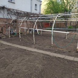 Szybki ogród - Konstrukcja z rurek i gałęzi w ogrodzie, przygotowana pod rośliny pnące, widoczna ziemia i kostka brukowa.