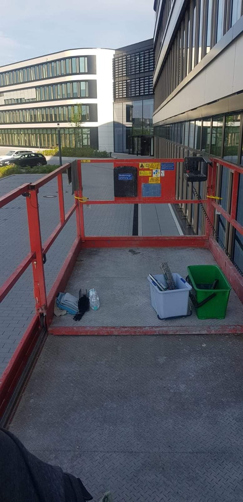Widok z platformy podnośnika koszowego na budynek biurowy z licznymi oknami, widoczne wiadra i narzędzia do czyszczenia.