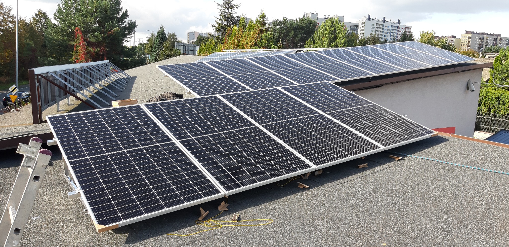 Montaż paneli fotowoltaicznych na dachu budynku w Rybniku, widoczna drabina oparta o panel oraz elementy konstrukcyjne pod panelami.