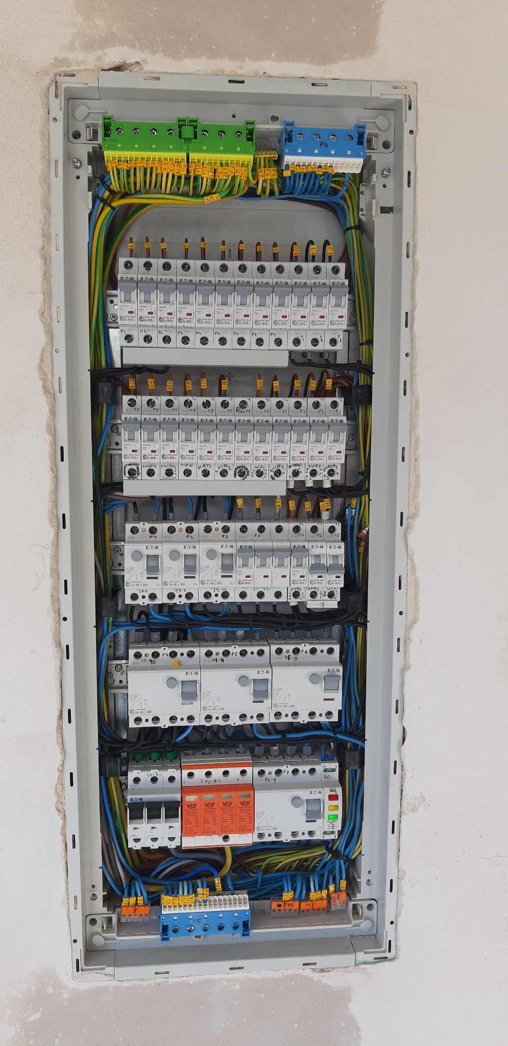 Rozdzielnica elektryczna z zamontowanymi bezpiecznikami, zabezpieczeniami przepięciowymi i listwami zaciskowymi, widoczne przewody w kolorach: żółto-zielonym, niebieskim i brązowym, montaż w nowym...