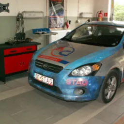 Kia Ceed z instalacją LPG marki STAG, zaparkowana w warsztacie, widoczny numer rejestracyjny B1 STAG i logo AC Spółka Akcyjna na masce.