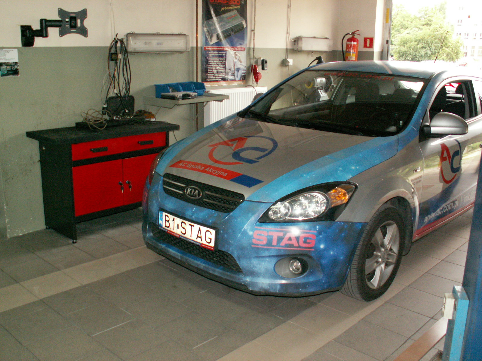 Kia Ceed z instalacją LPG marki STAG, zaparkowana w warsztacie, widoczny numer rejestracyjny B1 STAG i logo AC Spółka Akcyjna na masce.