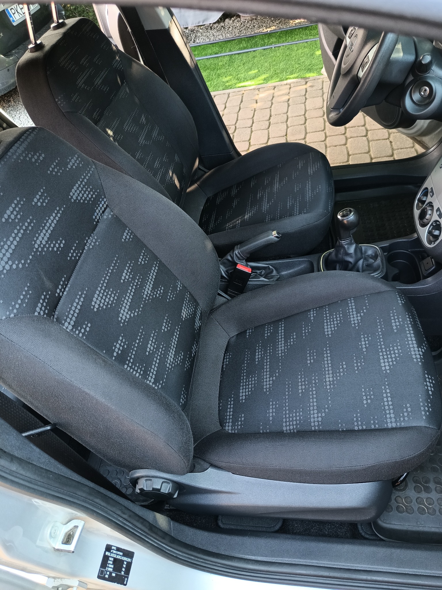 Wnętrze samochodu Opel Corsa: czarne fotele z geometrycznym wzorem, widoczna dźwignia zmiany biegów i hamulec ręczny.