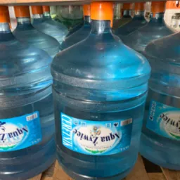 Baterie butli z wodą Aqua Żywiec 18.9L z pomarańczowymi nakrętkami, ustawione na drewnianej palecie, widoczne etykiety z nazwą i logo.