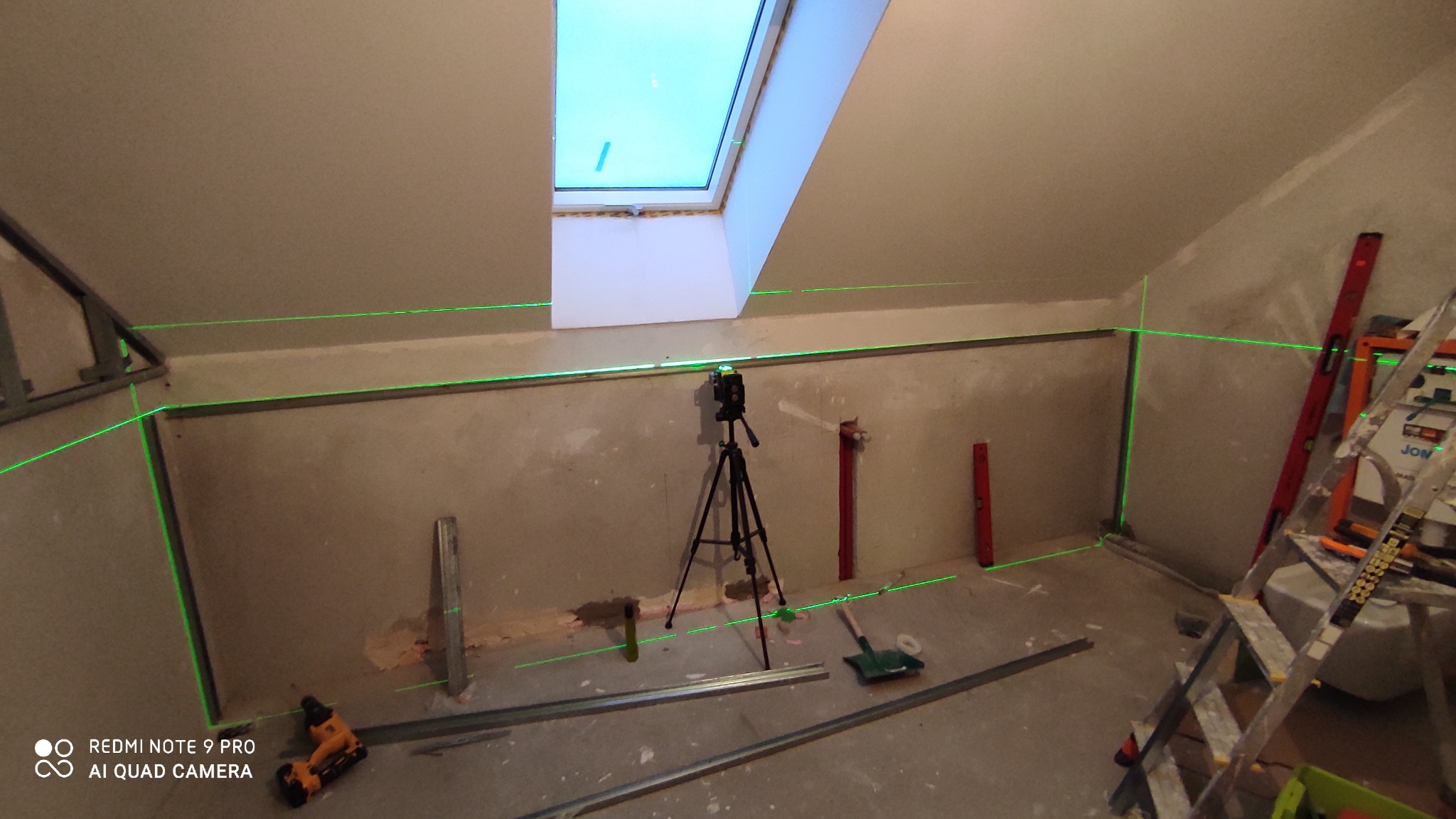 Montaż profili pod płytę karton gips w pokoju na poddaszu, wyznaczane laserowo, widoczny poziomica laserowa na statywie, w tle okno dachowe.