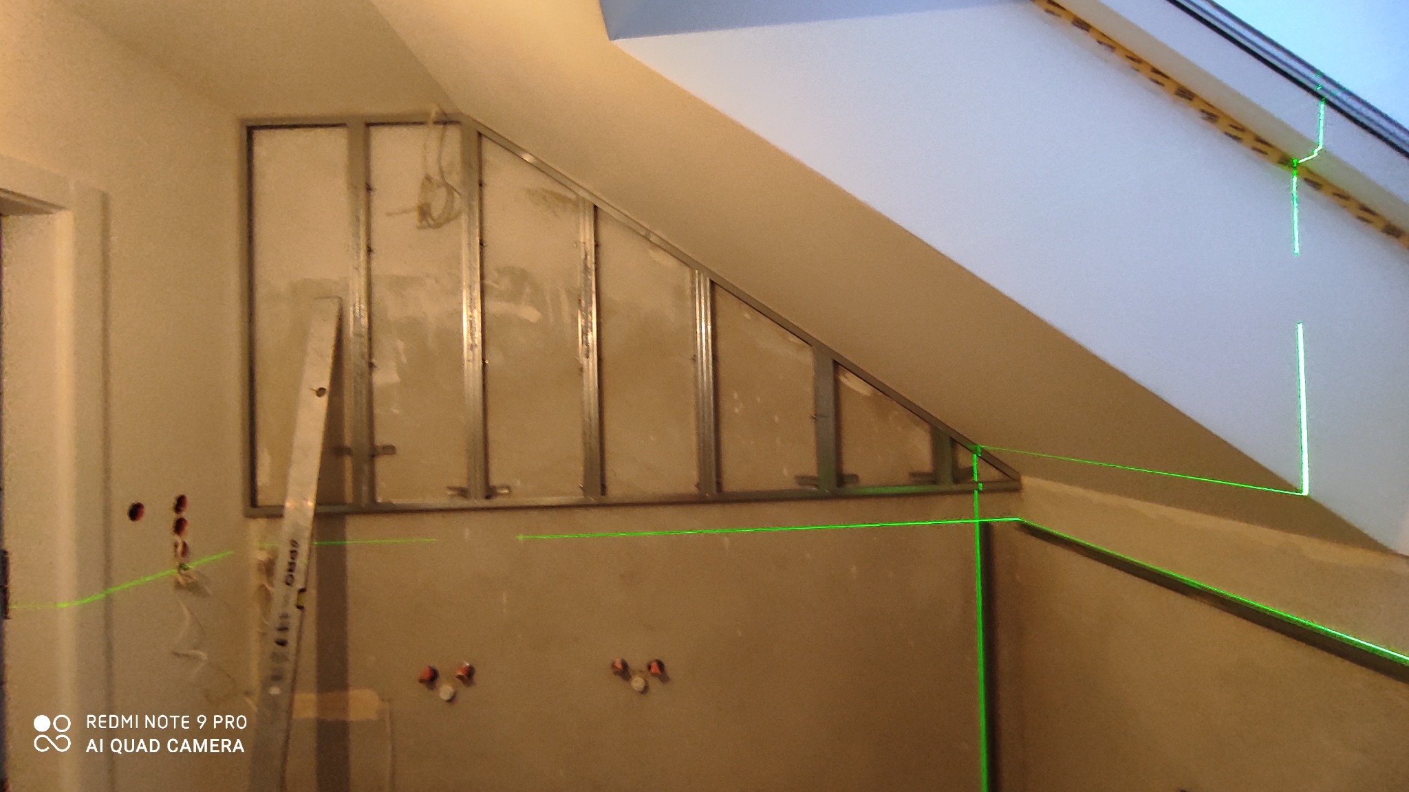 Montaż metalowej konstrukcji pod płytę karton-gips na poddaszu, widoczne profile, drabina aluminiowa i laserowy niwelator wyznaczający poziom.